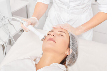 Beautician makes ultrasound skin tightening for rejuvenation woman face using phonophoresis, anti aging cosmetic procedure with in beauty spa salon. Cosmetologist makes ultrasonic skincare lifting