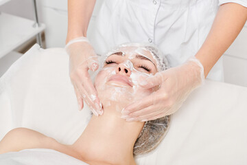 Beautician massages cream mask into female face skin for rejuvenation, moisturizing skincare...