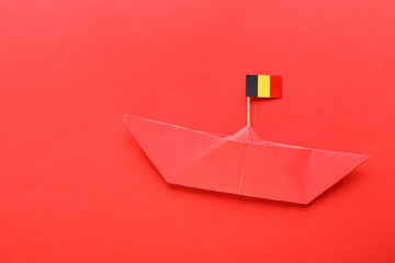 Paper ship and small flag of Belgium on red background