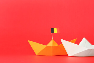 Paper ships and small flag of Belgium on red background, closeup
