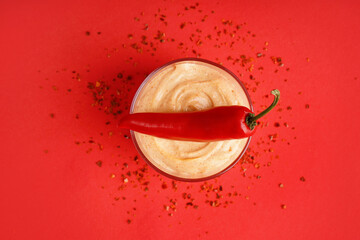 Bowl of tasty chipotle sauce and fresh jalapeno pepper on red background