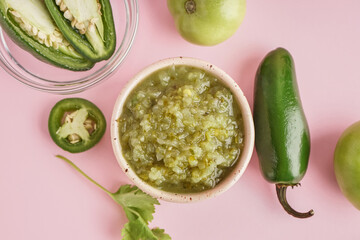 Bowl of tasty green salsa sauce and ingredients on pink background