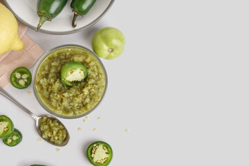 Bowl of tasty green salsa sauce and jalapeno peppers on light background - obrazy, fototapety, plakaty