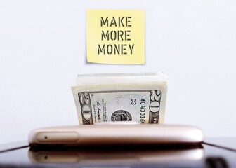 Mobile smartphone ,cash dollars money with wall sticky note MAKE MORE MONEY, refers to financial...