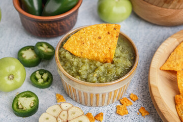 Bowl of tasty green salsa sauce with nacho on light background