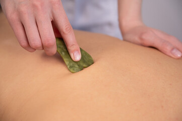 The masseur makes a back massage with a gouache scraper to a female client. 