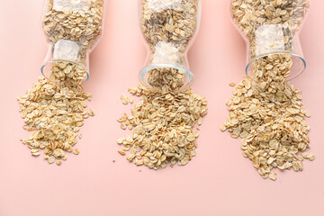 Overturned bottles of raw oatmeal on pink background, closeup