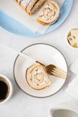 White plate with piece of delicious sponge cake roll, fork and cup of coffee on white table