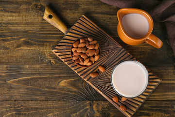 Fototapeta na wymiar Cutting board with glass of healthy almond milk and nuts on wooden background