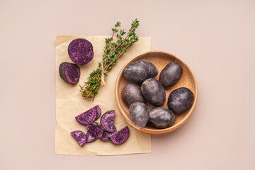 Wooden bowl with raw purple potatoes and thyme on color background