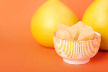 Bowl with slices of tasty pomelo fruit on orange background, closeup