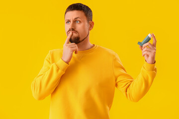 Thoughtful man with inhaler on yellow background