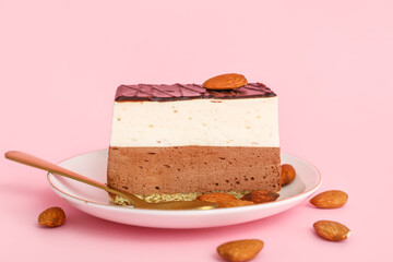 Plate with piece of birds milk cake, almond nuts and spoon on pink background