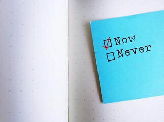 Blue note stick on notebook with text NOW or Never, concept of doing it now, take action to reach...