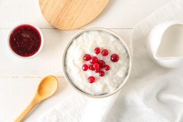 Bowl with delicious rice pudding, cranberry and jam on white wooden table