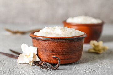 Obraz na płótnie Canvas Bowl with delicious rice pudding, floral decor and vanilla sticks on grey table