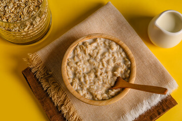 Bowl with tasty oatmeal, flakes in jar and pitcher on yellow background