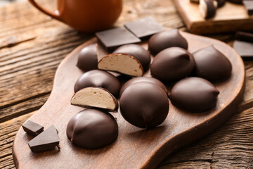 Cutting board with sweet chocolate bird's milk candies on wooden background, closeup