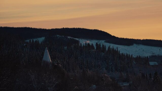 Shot of coniferous trees along the hilly slope covered with white snow in Beitostolen, village in Oystre Slidre Municipality in Innlandet county,Valdres, Beito, Norway with sunset.