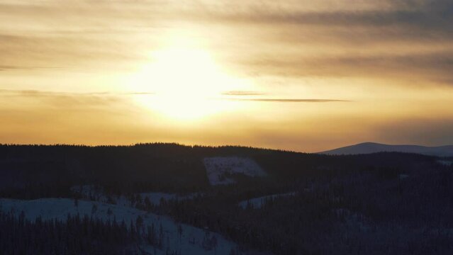 High angle shot over snow covered highlands with coniferous trees in Beitostolen, village in Oystre Slidre Municipality in Innlandet county, Valdres, Beito, Norway with sunset in background.