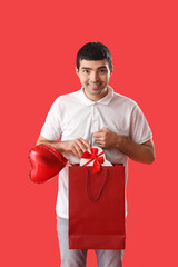 Young man with bag of gifts on red background. Valentine's Day celebration