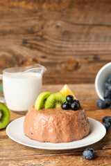 Plate with delicious chocolate pudding, blueberry, glass of milk, kiwi and lemon slices on wooden background