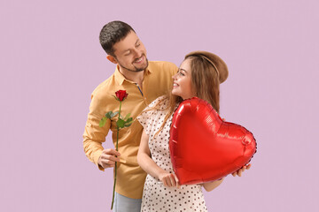 Happy young couple with heart-shaped balloon and flower on lilac background. Valentine's Day...
