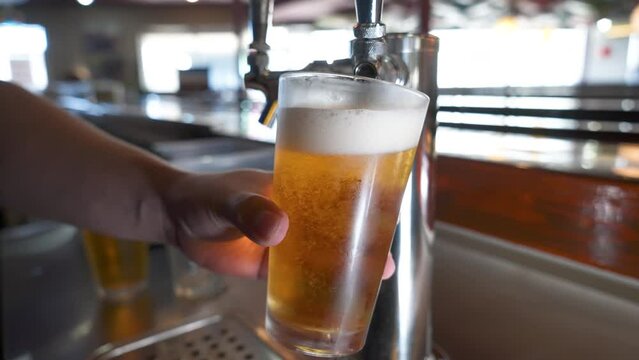 Bartender pulls a perfect pint from a stainless tap, frothy beer fills frosted pint glass, slow motion 4K