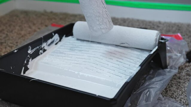 Close up of person rolling white paint on with a roller in a black tray.