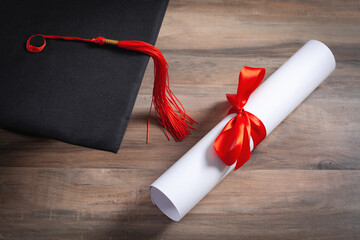 Graduation hat and diploma on the wooden background.
