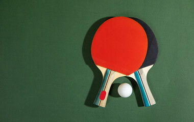 Table tennis rackets and a white plastic ball on the green background.