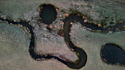 winding stream with ponds. people renewed the zigzagging cancel melioration, measures to maintain water in the landscape. a pond with a drowned tree is surrounded by lying frozen grass like fur