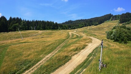 Summer mountain landscape with zipline and ski lift columns and mountain bike downhill dirt tracks, coniferous forest in background. Blue skies with scattered clouds. Location Kubinska Hola, Slovakia. © zayacsk