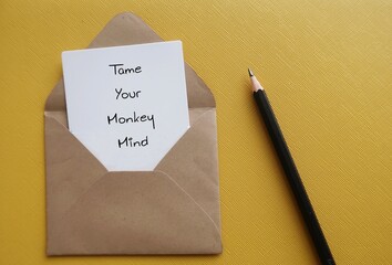 Pencil on yellow background with handwritten text card TAME YOUR MONKEY MIND, Buddhism mindfulness...