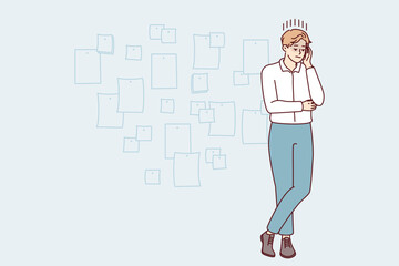 Young creative man project manager stands cross-legged and touches head thinking about future development of company. Startup employee guy posing near wall with stickers. Flat vector illustration