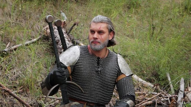 Smooth camera movement, selective focus, a man with gray hair and a scar on his face sits on a fallen tree with a two-handed sword in his hands. Medieval warrior, witcher in chainmail on a half.