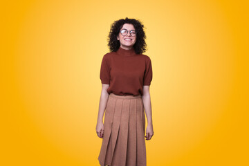 Young friendly woman wearing looking at camera and smiling standing against yellow background. Positive person. People lifestyle.