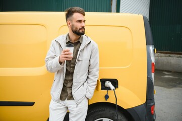 Casual man near electric car waiting for the finish of the battery charging process