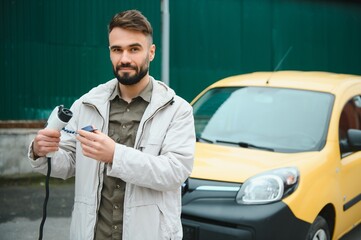 Stylish man inserts the charging cable into the socket of electric car