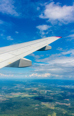 View of airplane wing, blue skies and green land during landing. Airplane window view.