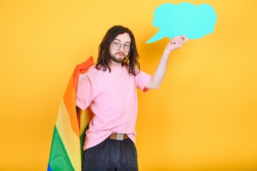 gay man with a gay pride flag smiling and looking away on yellow background.