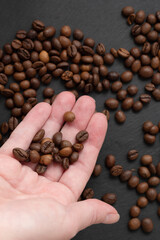 Roasted coffee beans on human hand palm on dark background