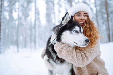 Happy woman walking her dog in the winter and both explore the snow together in playful mood. Friendship, pet and human.