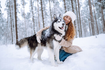 Naklejka premium Happy woman walking her dog in the winter and both explore the snow together in playful mood. Friendship, pet and human.