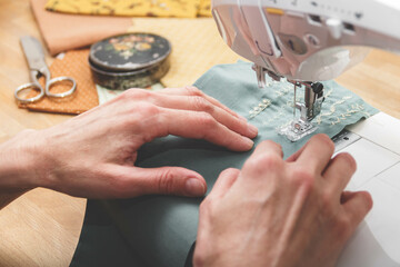 Tailoring Process - Women's hands with her sewing. Close up view of sewing process. Female hands stitching fabric on manufacturing machine at workplace.