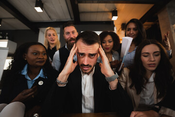Close-up young businessman stressed because overworked. Male sitting at desk with colleague putting...