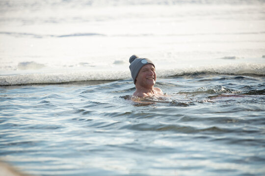 A man in warm hat swimming in an ice hole. Winter activity in Finland. Healthy lifestyle