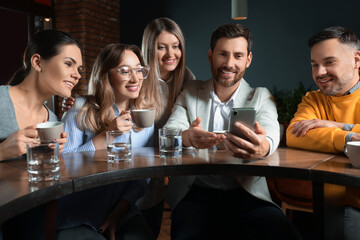 Handsome man showing something funny in smartphone to his friends in cafe