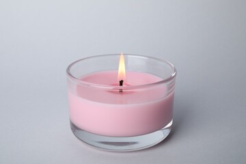 Fototapeta na wymiar Burning candle in glass holder on light grey background