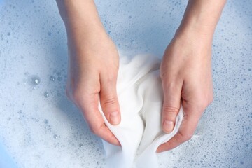 Top view of woman hand washing white clothing in suds, closeup